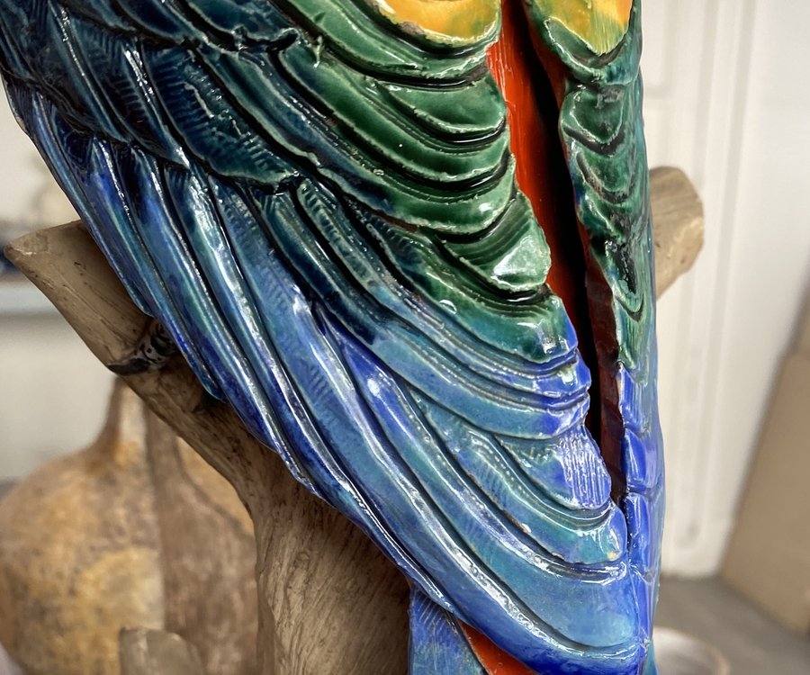 Détail d'un perroquet en céramique polychrome : la cassure court le long du plumage